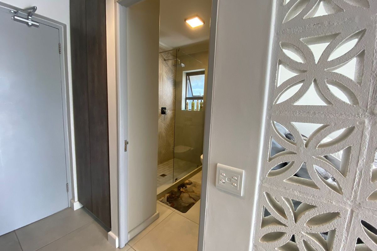 A view into a modern bathroom featuring a glass-enclosed shower, tiled finishes, and a decorative breeze block partition wall.