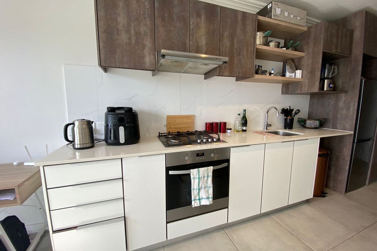 Modern kitchen featuring built-in cabinetry, stone countertops, gas hob, integrated oven, and a sleek tiled backsplash in a contemporary apartment setting.