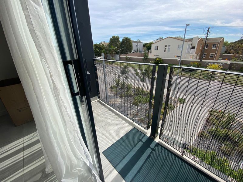 A modern apartment balcony featuring a metal mesh balustrade and tiled flooring, accessible via a large sliding glass door.
