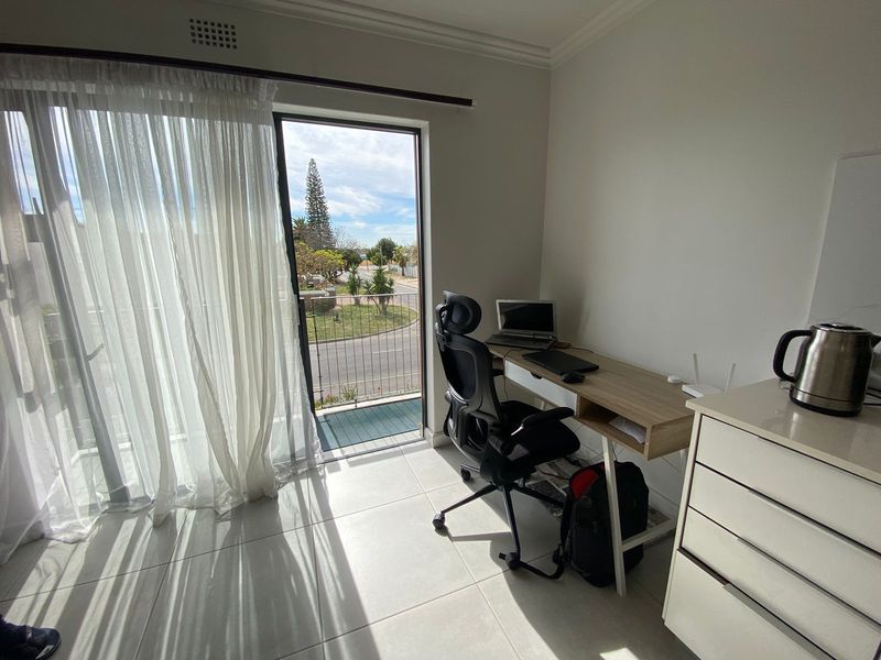 A bright home office space featuring tiled flooring and a sliding glass door providing direct access to a balcony.