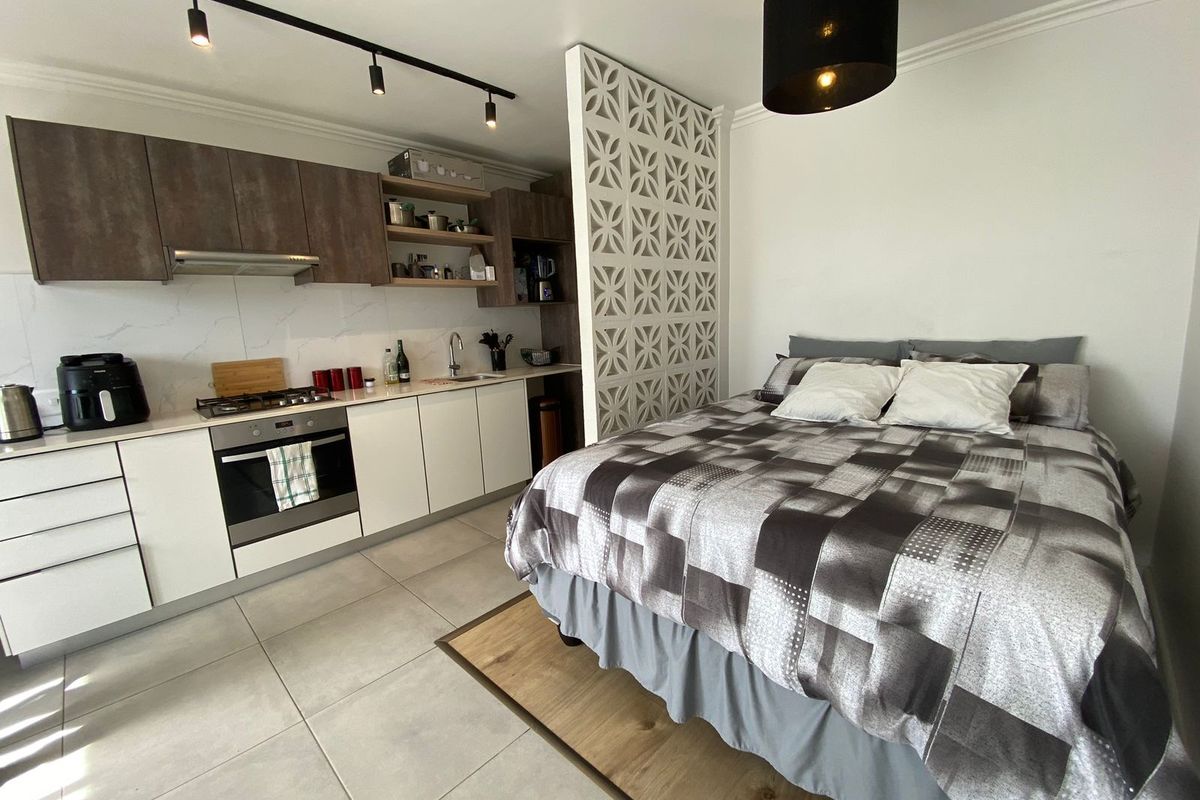 Modern open-plan studio apartment featuring a compact kitchen with built-in appliances, decorative partition wall, and tiled flooring throughout.
