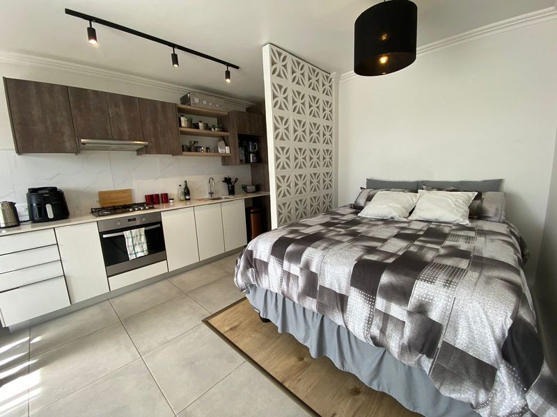 Modern open-plan studio apartment featuring a compact kitchen with built-in appliances, decorative partition wall, and tiled flooring throughout.