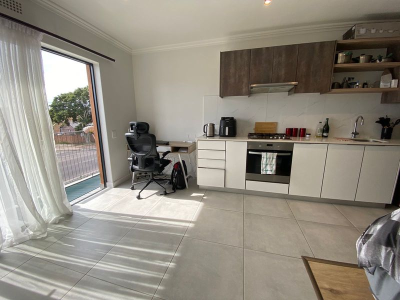 Modern open-plan kitchen featuring sleek cabinetry, integrated appliances, and large format floor tiles, with direct access to a private balcony.