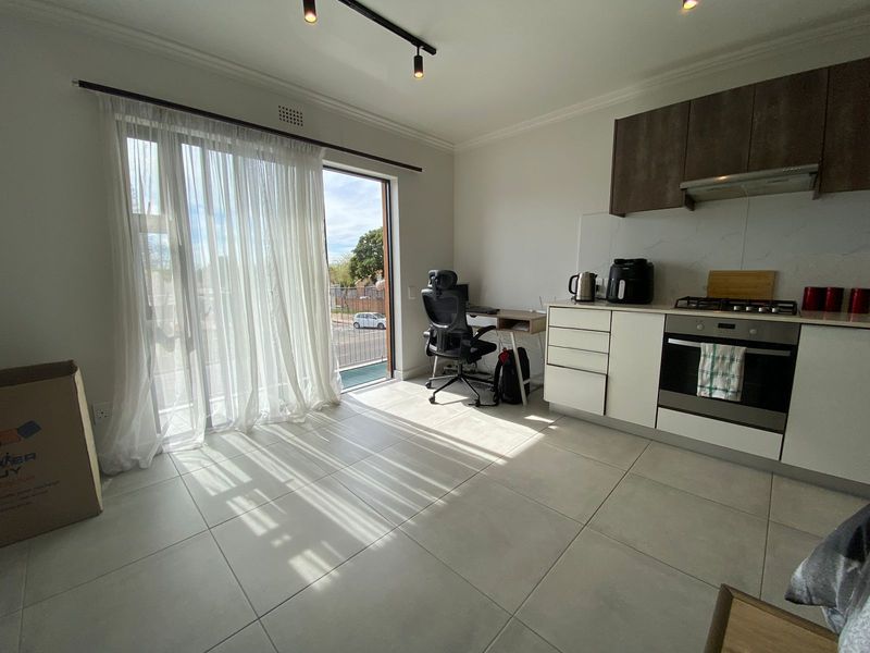 Modern open-plan kitchen and living area featuring tiled floors, built-in cabinetry, integrated appliances, and a sliding door leading to a balcony.