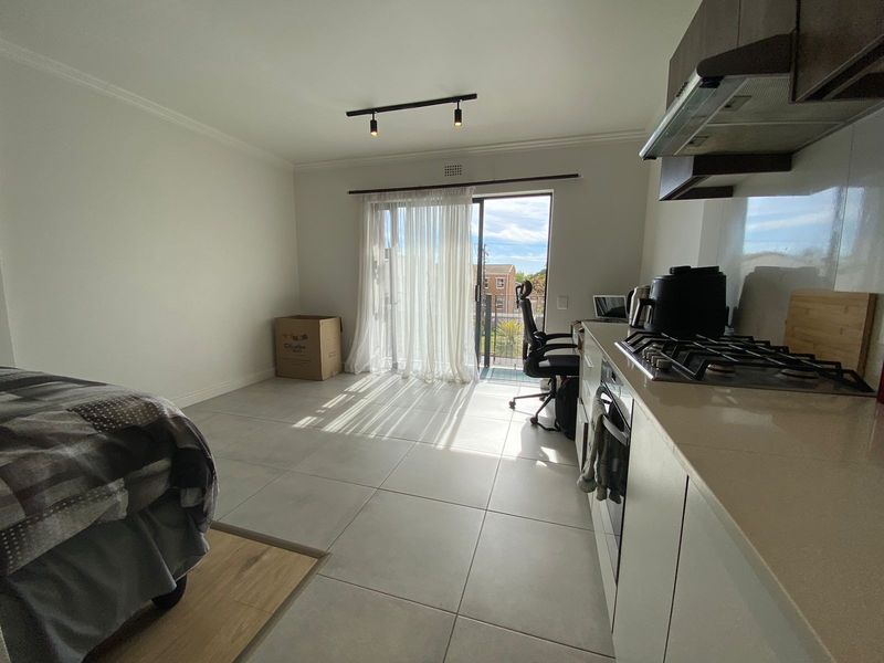 Open-plan living area featuring tiled flooring, a modern kitchen with gas hob and extractor, and sliding door access to a balcony.