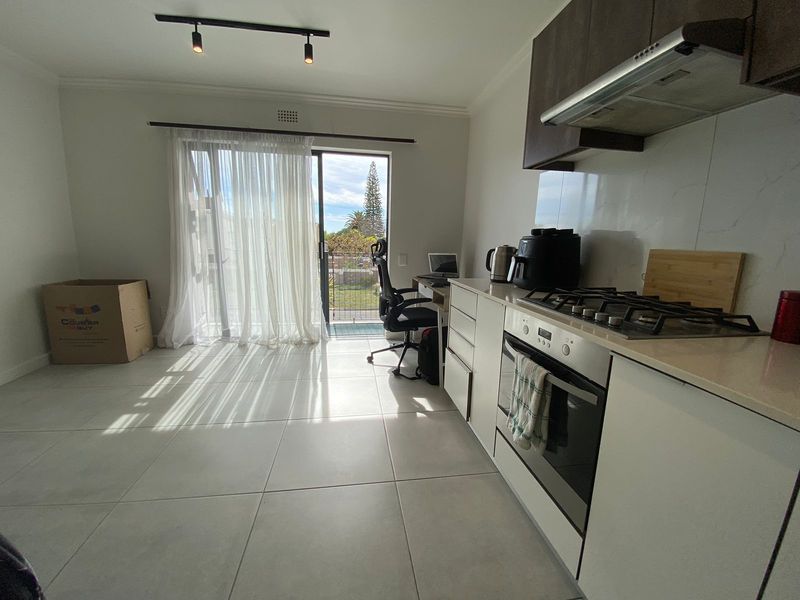 Open-plan kitchen and living area featuring modern cabinetry, gas hob, built-in oven, and direct access to a balcony through sliding glass doors.