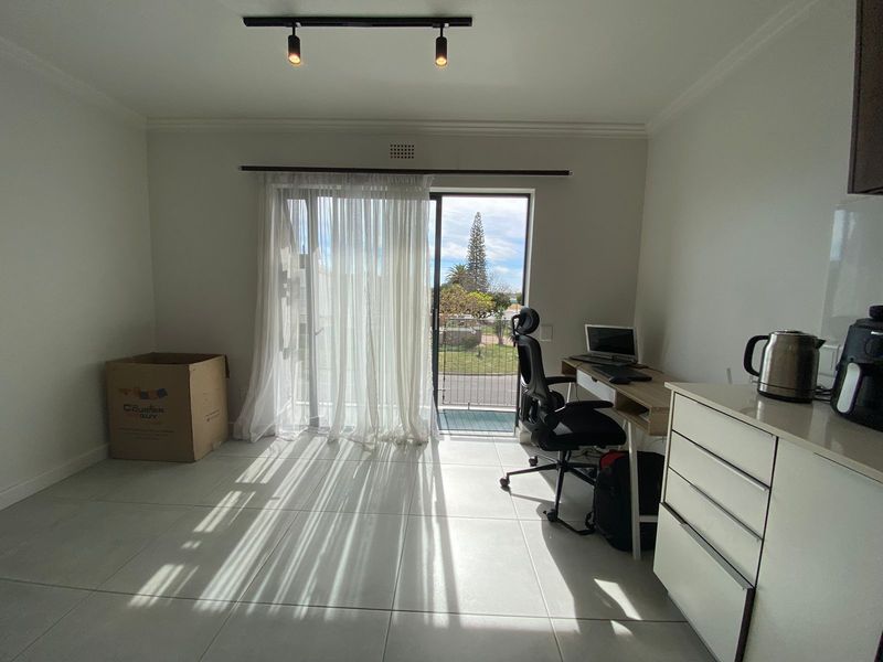 Open plan living area featuring tiled floors, modern track lighting, and a sliding glass door leading to a balcony with natural light.