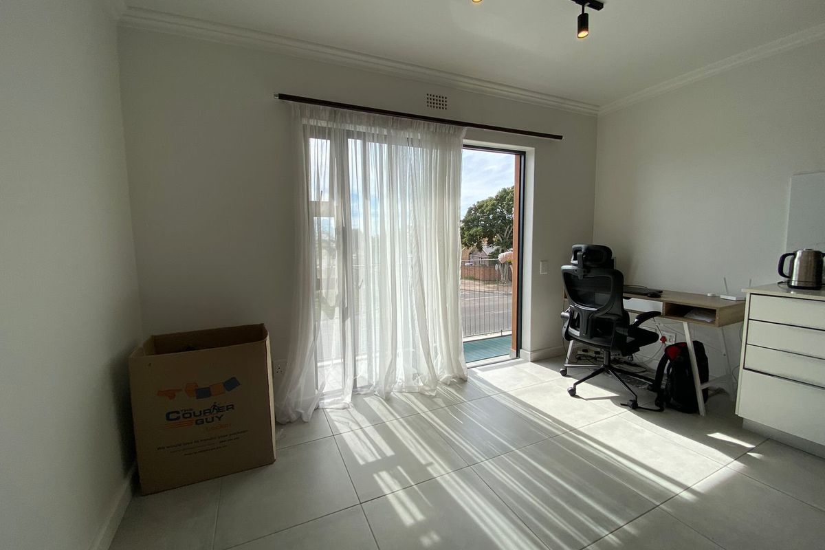 A bright bedroom featuring large sliding glass doors that open to a balcony, neutral tiled flooring, and modern track lighting.