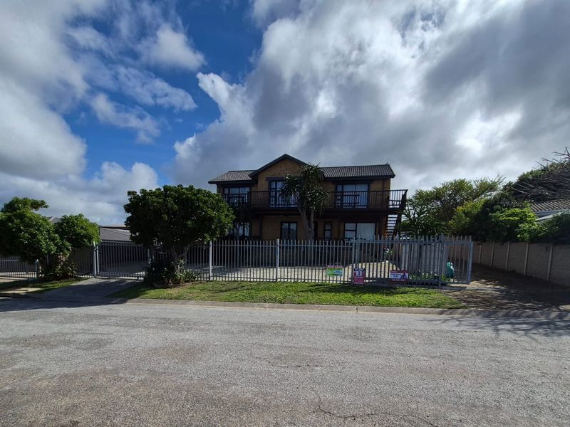 Front view of a two-story brick house featuring a balcony, paved driveway, and secure metal perimeter fencing.