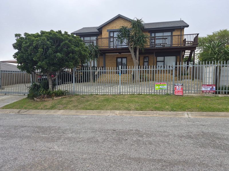 A two-story brick house featuring a timber balcony, paved driveway, and secure steel fencing, presenting a well-maintained exterior facade.