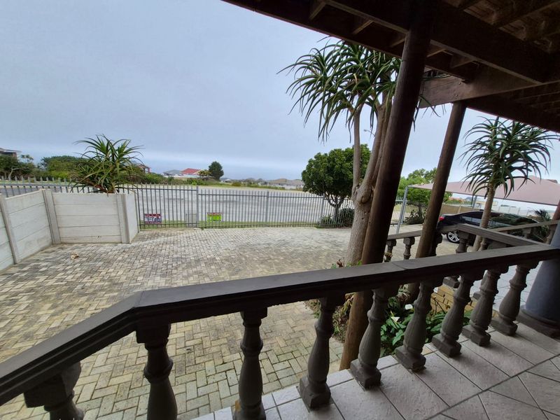 A covered balcony with a wooden balustrade overlooking a paved driveway and fenced perimeter.