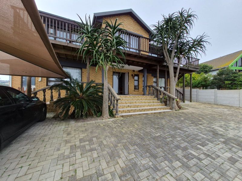 Front elevation of a two-story brick house featuring a paved driveway, elevated timber balcony, and concrete balustrade staircase entrance.