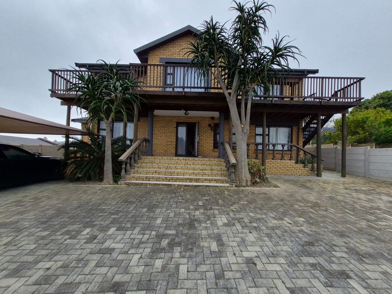 A two-story brick house featuring a large wooden balcony, a paved driveway, and a prominent front staircase entrance.