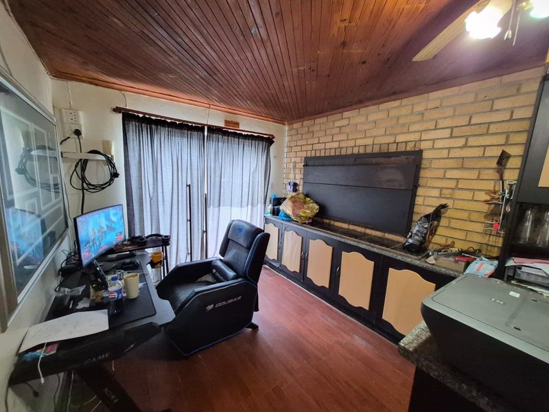 A living area featuring a timber ceiling, exposed brick wall, and a built-in braai, with sliding door access to the exterior.