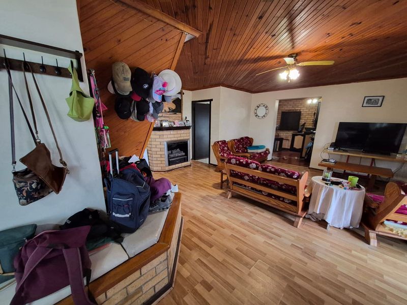 Spacious living room featuring a brick fireplace, timber-clad ceiling, and laminate flooring, offering a warm and functional layout.
