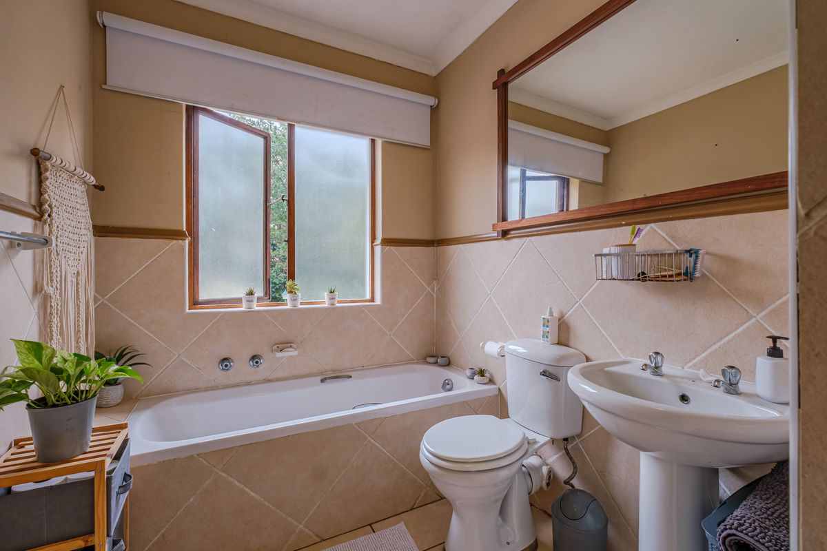 A functional bathroom featuring a bathtub, pedestal sink, toilet, and a large wall-mounted mirror with neutral tiled wall finishes.