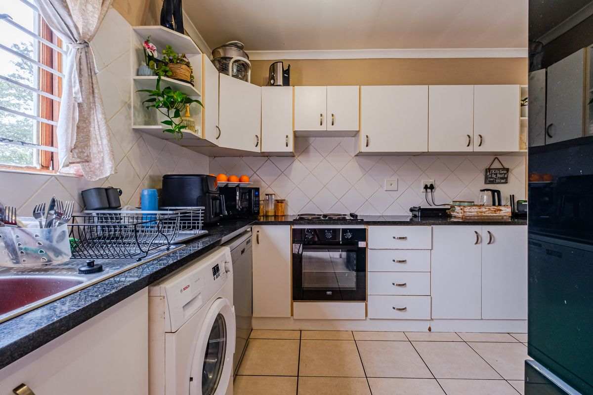 A functional kitchen featuring white cabinetry, dark laminate countertops, a built-in oven, and tiled flooring with space for laundry appliances.