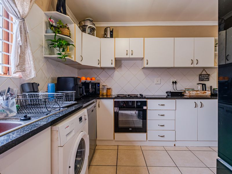 A functional kitchen featuring white cabinetry, dark laminate countertops, a built-in oven, and tiled flooring with space for laundry appliances.
