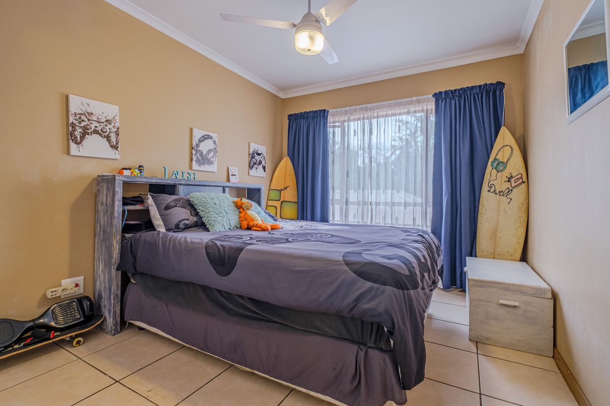 A bedroom featuring tiled flooring and a ceiling fan, with large windows dressed in curtains.