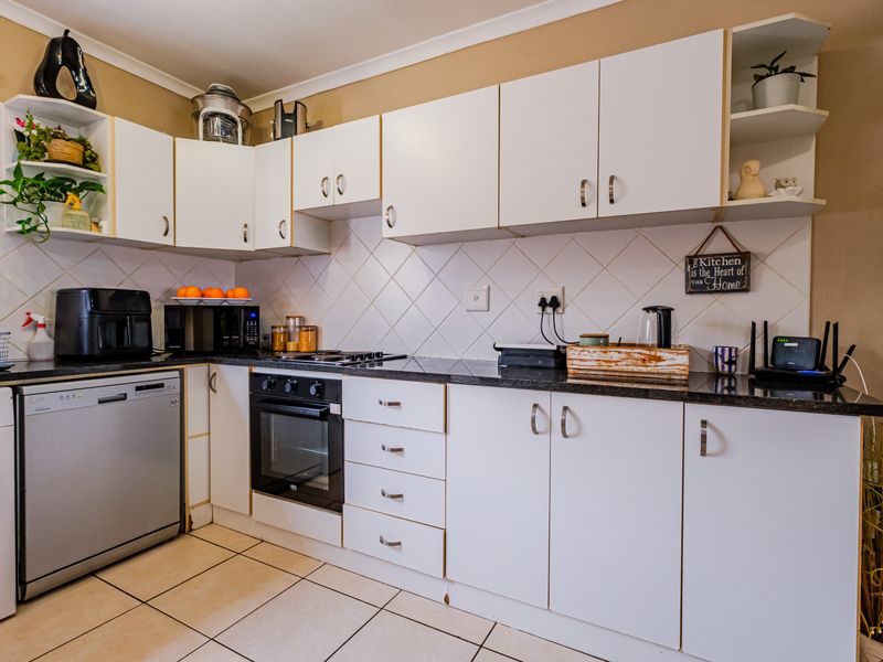 A functional kitchen featuring white cabinetry, granite countertops, a tiled backsplash, and built-in oven and hob, with tiled flooring throughout.