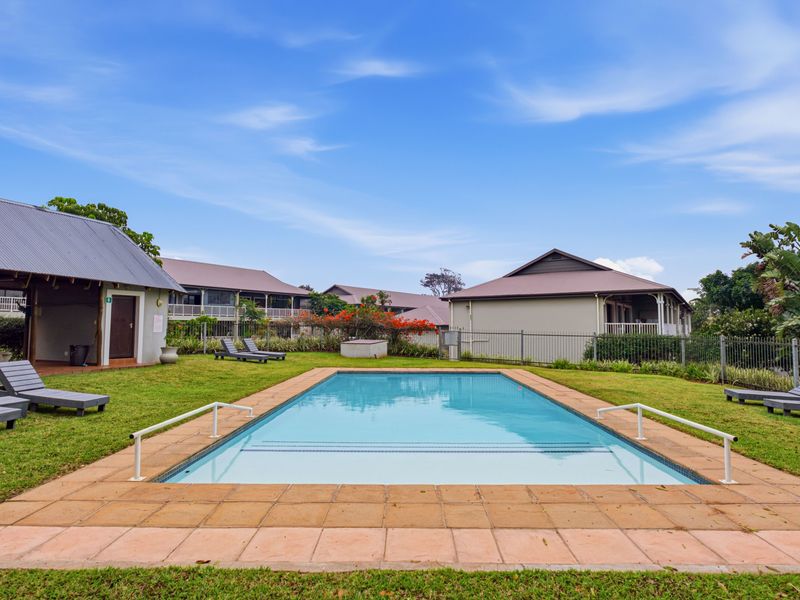 A well-maintained outdoor swimming pool area featuring paved coping, safety handrails, and surrounding lawn within a residential complex.