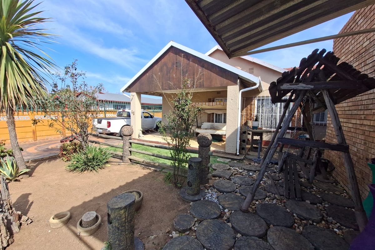 Rear view of the property featuring a covered patio area, brick facade, and a landscaped garden with a paved stone pathway.