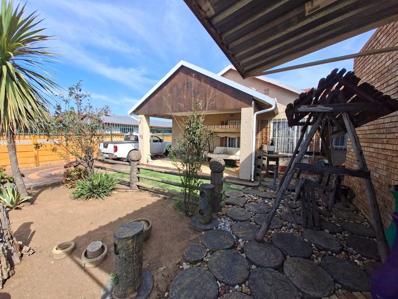 Rear view of the property featuring a covered patio area, brick facade, and a landscaped garden with a paved stone pathway.