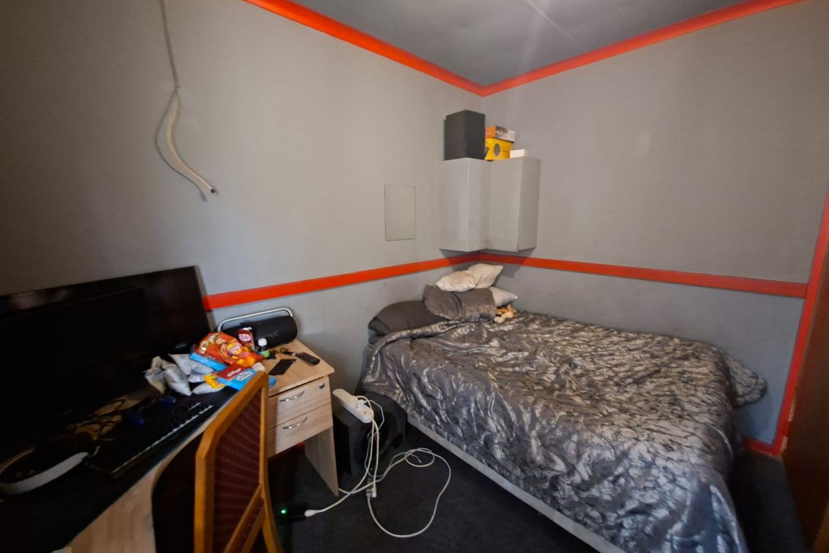 A compact bedroom featuring grey walls with orange trim accents and built-in corner shelving, requiring cosmetic updates to improve the overall aesthetic.