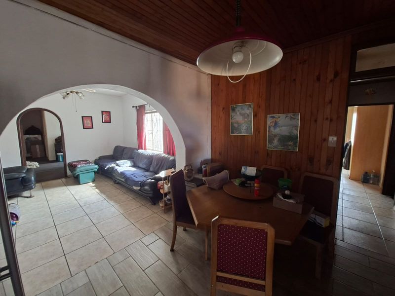 Open plan living and dining area featuring timber ceiling and wall paneling, ceramic tiled flooring, and a distinctive arched architectural transition.