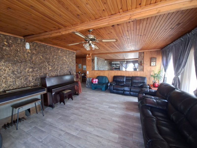Spacious living room featuring a timber-clad ceiling, tiled flooring, and a textured feature wall, offering a warm and traditional aesthetic.