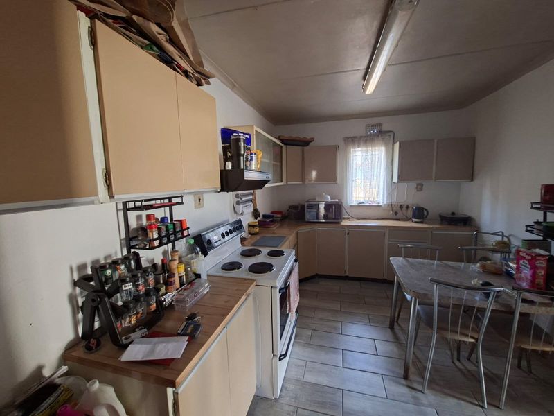 A functional kitchen featuring built-in cabinetry, an electric stove with extractor fan, and tiled flooring, offering potential for modernization and aesthetic updates.