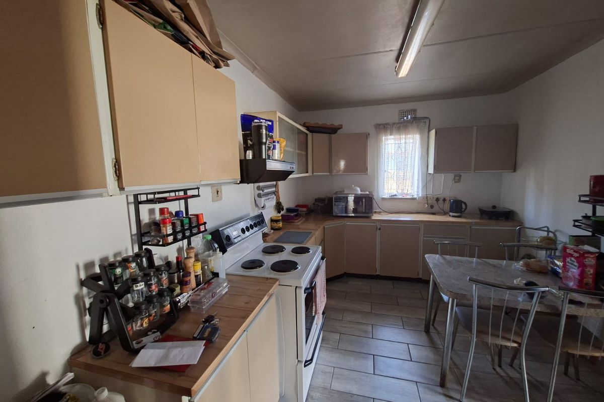 A functional kitchen featuring built-in cabinetry, an electric stove with extractor fan, and tiled flooring, offering potential for modernization and aesthetic updates.