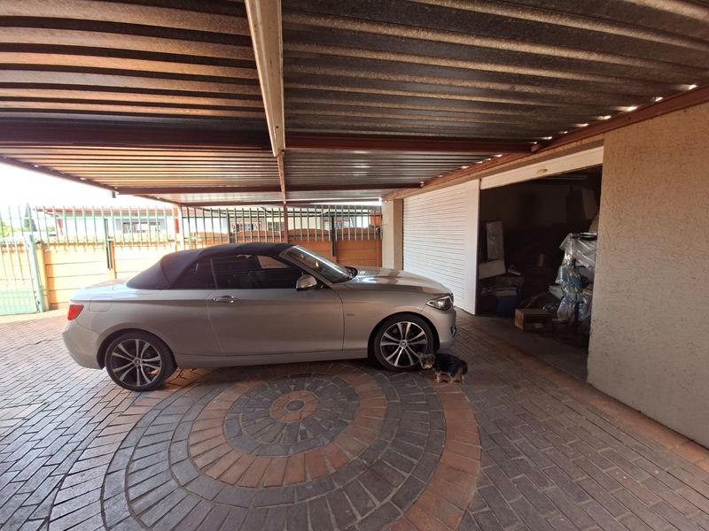 A covered carport area featuring a paved driveway and a roller shutter door leading into a storage or garage space.