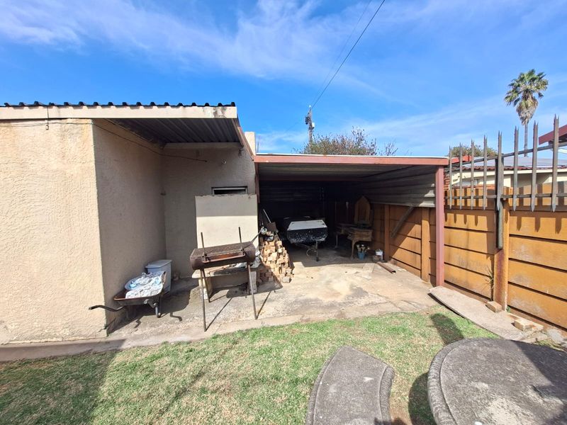 Rear exterior view featuring a covered patio area with concrete flooring, metal roofing, and perimeter steel fencing.