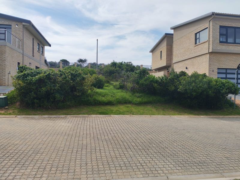 Vacant residential plot situated between two existing multi-story brick dwellings, featuring established landscaping and paved street access.