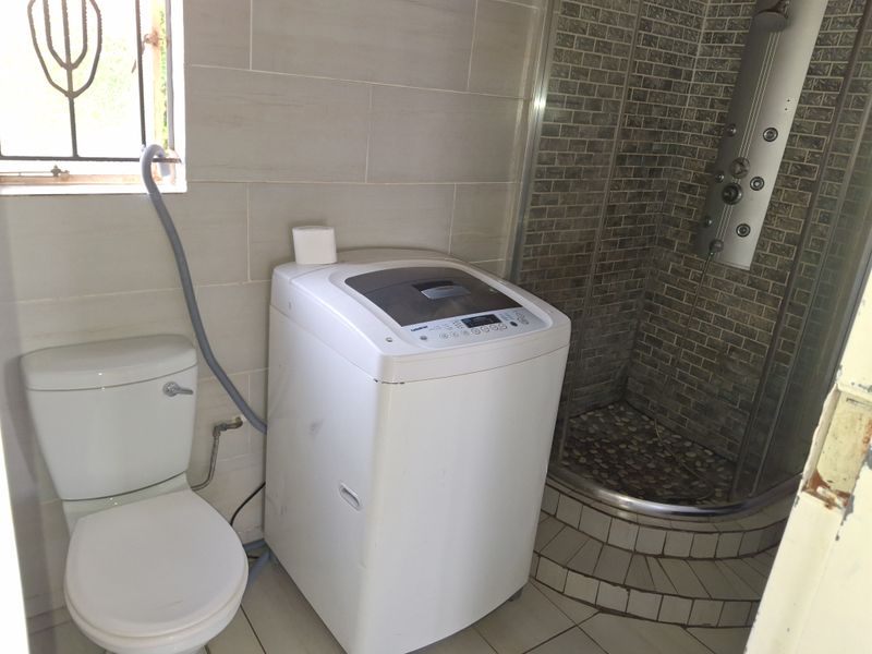 A functional bathroom featuring a toilet, a shower enclosure with a modern shower panel, and tiled finishes throughout.