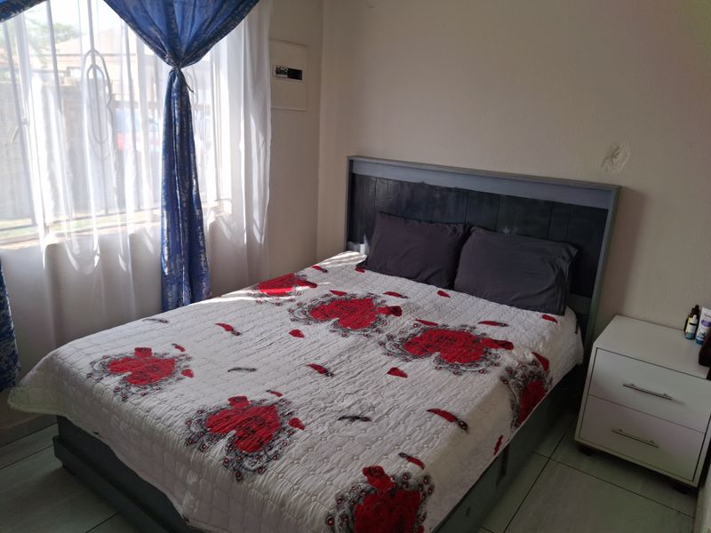 A functional bedroom featuring tiled flooring and a wall-mounted electrical distribution board, with visible wall surface imperfections requiring minor repair.