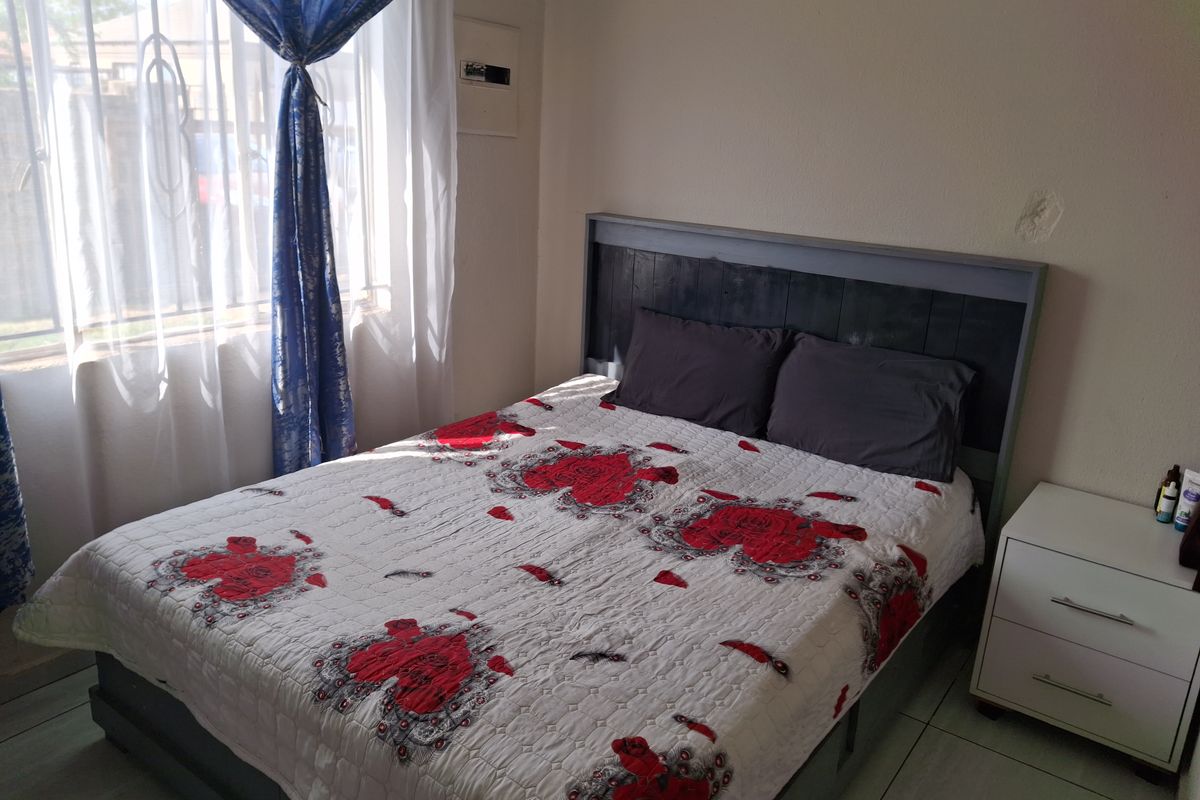 A functional bedroom featuring tiled flooring and a wall-mounted electrical distribution board, with visible wall surface imperfections requiring minor repair.