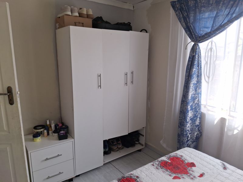 A bedroom featuring tiled flooring and a window with a security gate, showing signs of wall surface wear and peeling paint.