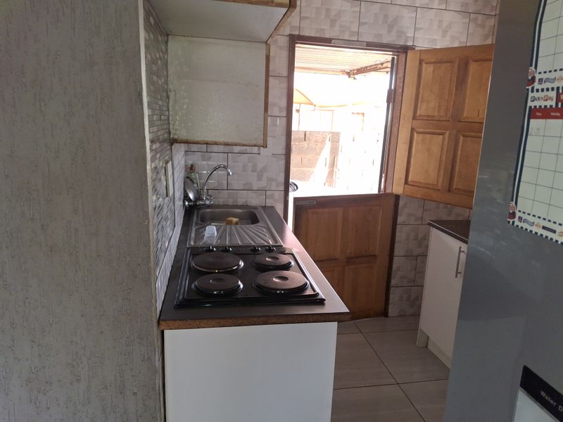 Compact kitchen featuring a built-in electric hob, stainless steel sink, tiled splashbacks, and direct access to the exterior via a stable door.