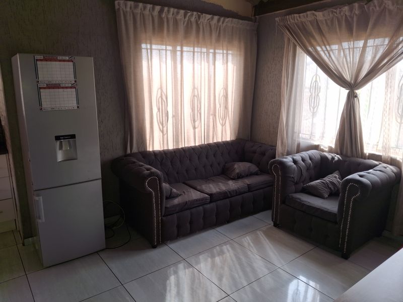 A living room area featuring tiled flooring, textured wall finishes, and windows secured with burglar bars.