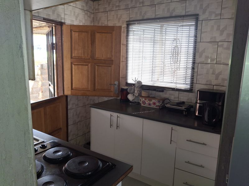 A functional kitchen featuring white cabinetry, dark laminate countertops, an electric hob, and a stable door leading to the exterior.