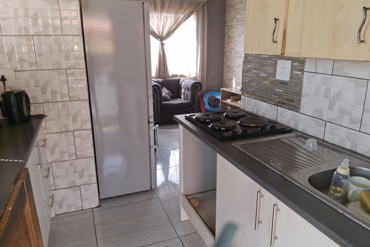 A compact kitchen featuring tiled splashbacks, a built-in electric hob, and stainless steel sink, with some cabinetry requiring maintenance or replacement.
