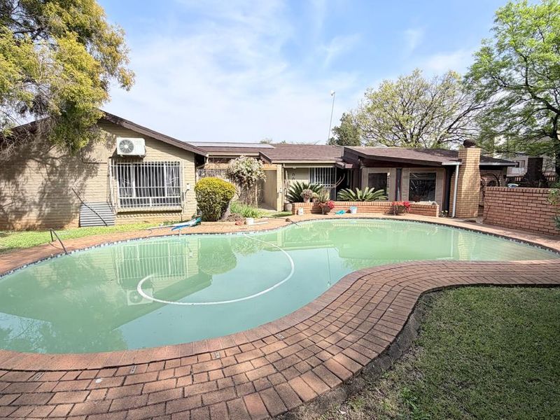 Rear exterior view featuring a swimming pool with brick surround, brick chimney, and established garden setting.