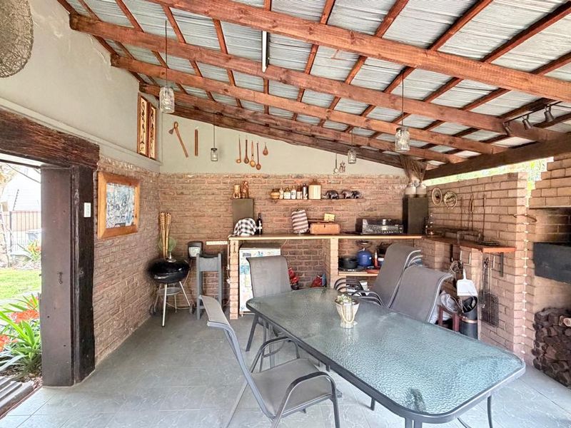 Covered outdoor patio featuring exposed timber beams, brick walls, and a built-in fireplace, providing a rustic space for outdoor entertaining.