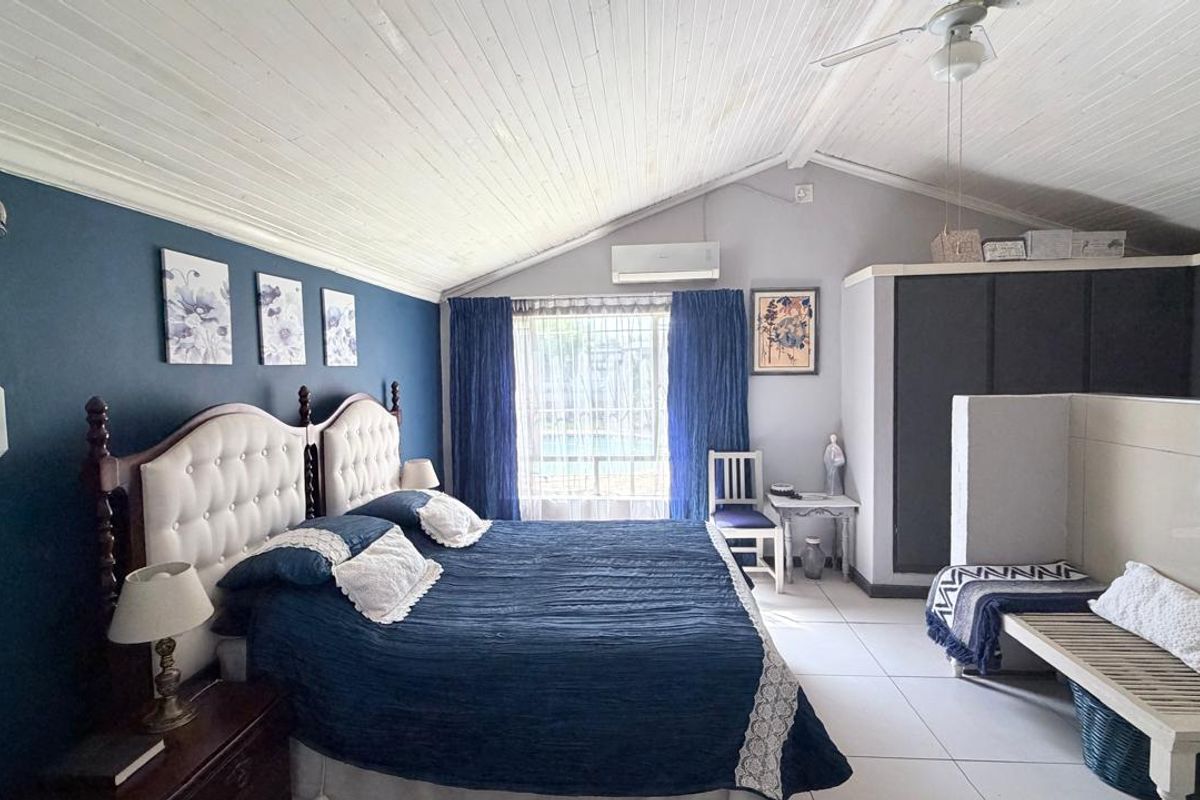 Spacious bedroom featuring a vaulted timber ceiling, tiled flooring, built-in cupboards, and a split-system air conditioner for climate control.