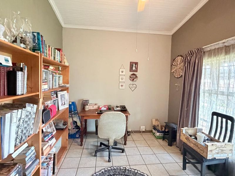 A functional home office space featuring tiled flooring, a ceiling fan, and natural light from a large window.