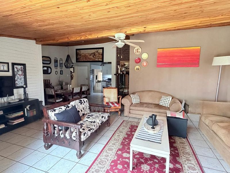 Open plan living and dining area featuring a timber ceiling, ceiling fan, tiled flooring, and a brick fireplace.