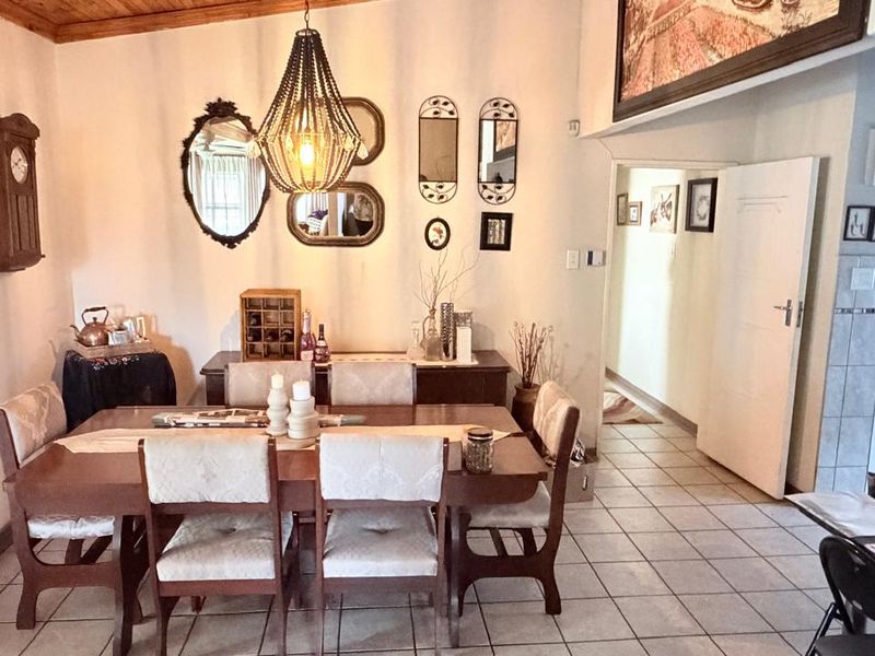 A dining room featuring tiled flooring and a timber ceiling, with an open transition leading to a hallway and kitchen area.