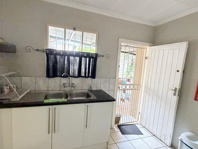 A functional scullery area featuring a double bowl sink, tiled backsplash, laminate countertop, and direct access to the exterior via a security gate.